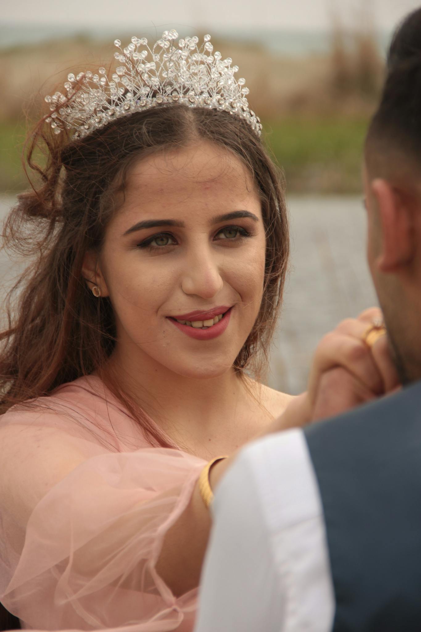 A young woman wearing a tiara holds hands with a partner outdoors, exuding a sense of elegance and connection.